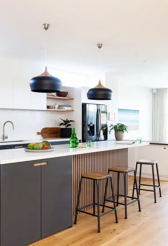 a lovely contemporary kitchen with graphite grey and white cabinets, a white chevron tile backsplash, catch black pendant lamps