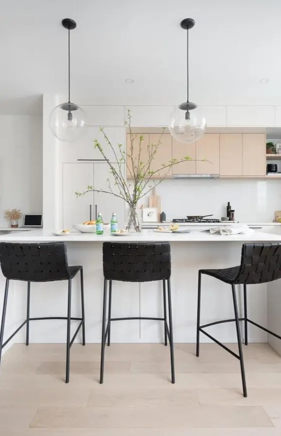 a lovely contemporary kitchen with white and stained cabinets, a white kitchen island, black woven stools, pendant lamps