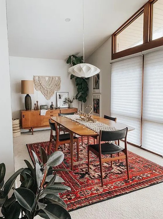 a lovely mid century modern dining room with a credenza, a stained table, black chairs, a faceted pendant lamp and a bold printed rug