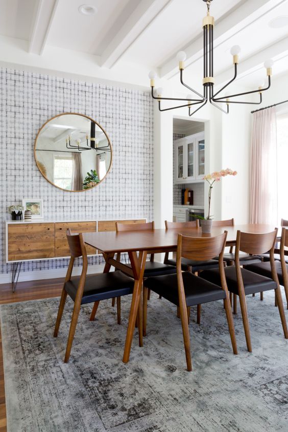 a lovely mid-century modern dining space with a stained credenza, a stained table and black chairs, a stylish chandelier and a round mirror