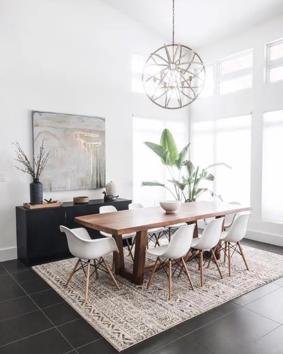 a mid century modern dining space with a stained table and white Eames chairs, a printed rug, a black credenza, a sphere chandelier and potted plants