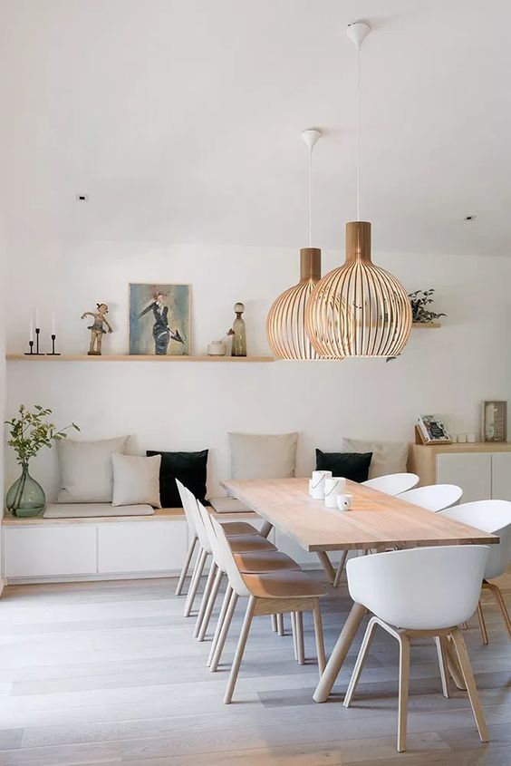 a minimal Scandinavian dining room with a storage bench with pillows, a stained table and white chairs, wooden pendant lamps