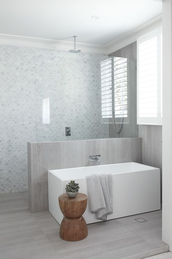 a minimalist bathroom with a half wall with glass to separate the shower space, a rectangle tub and a wooden side table