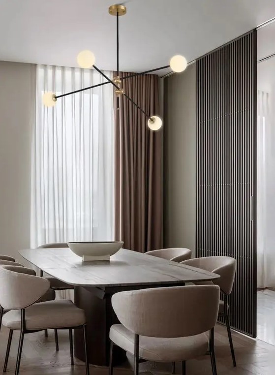 a minimalist greige dining room with a large table, beige chairs, a chic mid century modern chandelier and taupe curtains