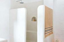 a modern Moroccan-inspired bathroom with a shower space done with half walls, candle lanterns, a rug and towels