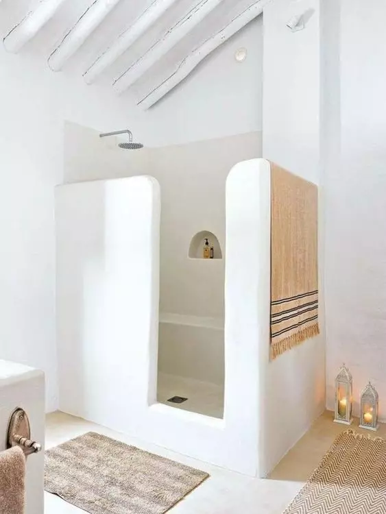 a modern Moroccan-inspired bathroom with a shower space done with half walls, candle lanterns, a rug and towels