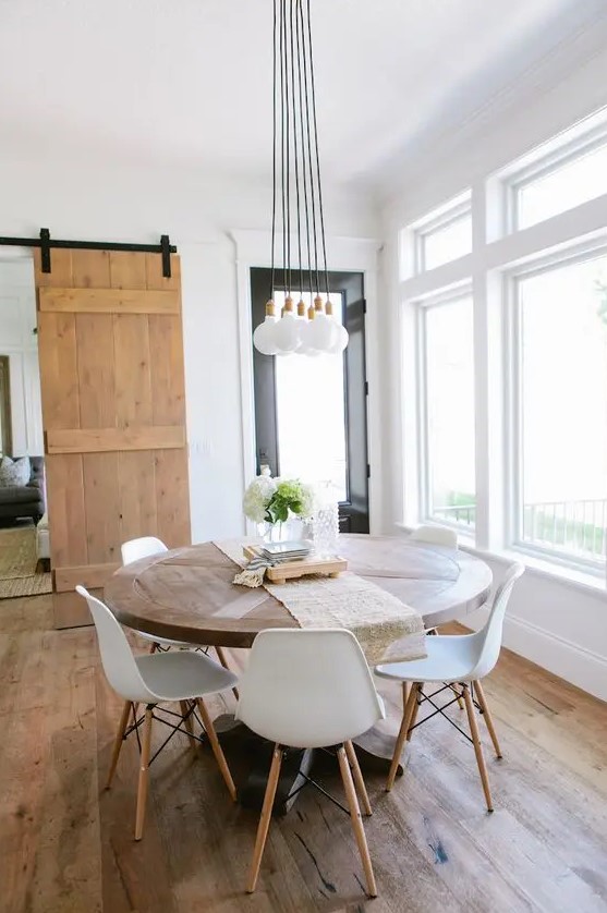 a modern Scandi dining room with a round table, white chairs, a cluster of pendant lamps and greenery plus lots of natural light
