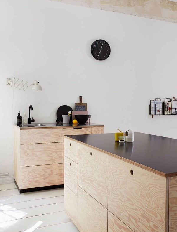 a modern kitchen with plywood and timber no hardware cabinets, black countertops and black fixtures, a black round clock
