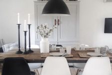 a monochromatic Scandinavian dining space with a stained table, black and white chairs, a black pendant lamp and a neutral storage unit