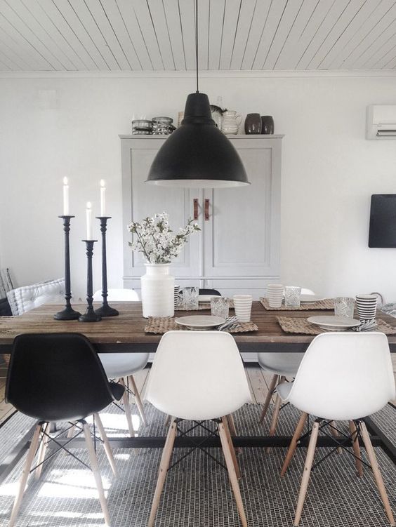 a monochromatic Scandinavian dining space with a stained table, black and white chairs, a black pendant lamp and a neutral storage unit