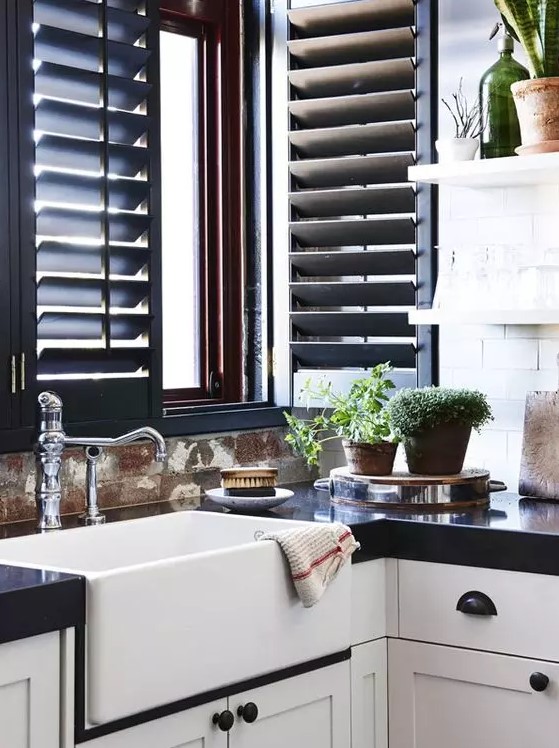 a monochromatic kitchen with white shaker style cabinets and black countertops, black shutters that match and add color and vintage fixtures