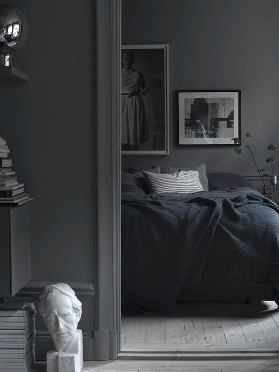 a moody Nordic bedroom with grey walls, a monochromatic gallery wall, dark bedding and potted greenery