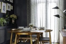 a moody mid-century modern dining space with a stained table and matching chairs, a black credenza, a stained cabinet with black lamps and a gallery wall