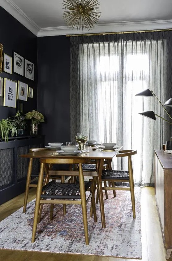 a moody mid-century modern dining space with a stained table and matching chairs, a black credenza, a stained cabinet with black lamps and a gallery wall