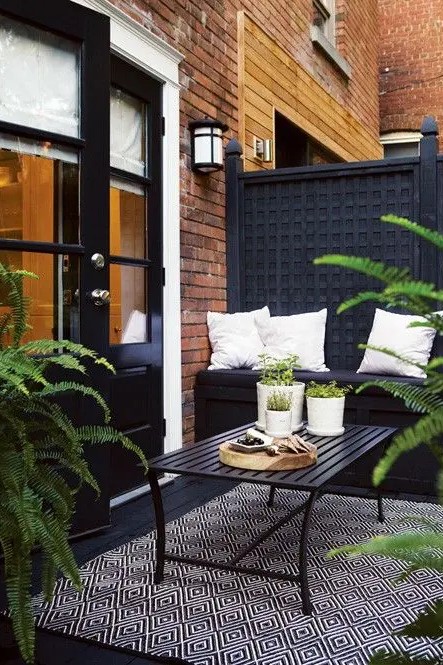 a moody small terrace with black furniture, rugs and lots of potted greenery to refresh the space