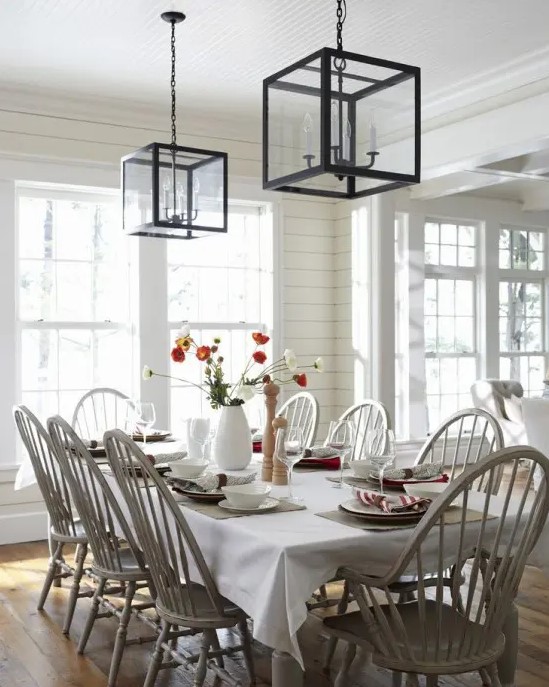 a neutral and very cozy dining room with planked walls, a table, wooden stained chairs, pendant lamps and a chic tablescape
