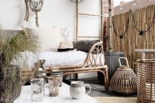 a neutral boho terrace with a rattan daybed, rattan candle lanterns and a white low coffee table, potted greenery and trees