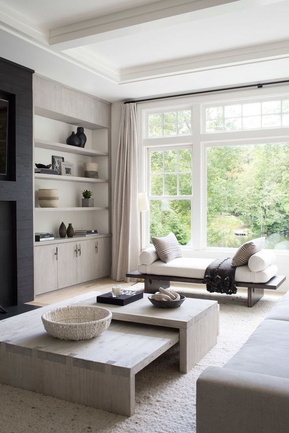 a neutral contemporary living room with a black fireplace, built-in shelves and cabinets, a duo of coffee tables, a neutral sofa and a daybed