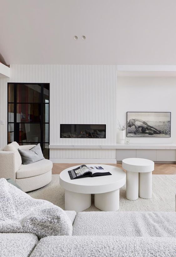 a neutral contemporary living room with a ribbed accent wall, a built-in fireplace, round coffee tables and a chair, a grey sofa