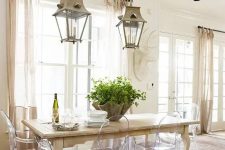 a neutral dining room with a wooden table and ghost chairs, pendant lamps, neutral textiles and some greenery