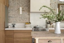 a neutral farmhouse kitchen with elegant and sleek no hardware cabinets, a large kitchen island, a large sleek hood and some blooming branches for decor