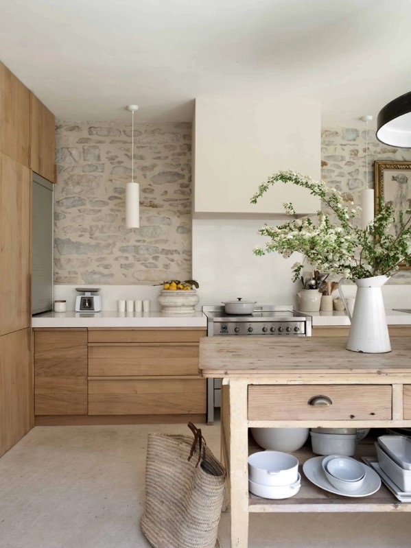 a neutral farmhouse kitchen with elegant and sleek no hardware cabinets, a large kitchen island, a large sleek hood and some blooming branches for decor