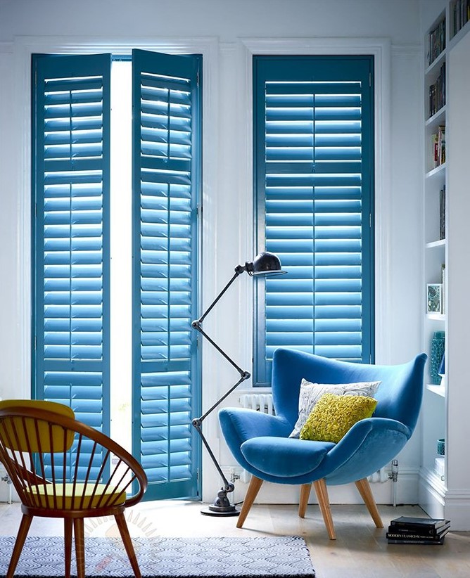 a neutral living room with built-in bookshelves and a blue chair by the window that is echoed in the color of the shutters