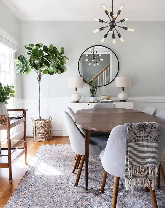 a neutral modern dining space with a stained wooden table, grey chirs, a bar cart, a round table, some potted greenery