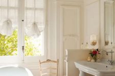 a neutral vintage bathroom with a vintage tub, a half wall that separates the toilet zone from the rest of the space, vintage curtains and furniture