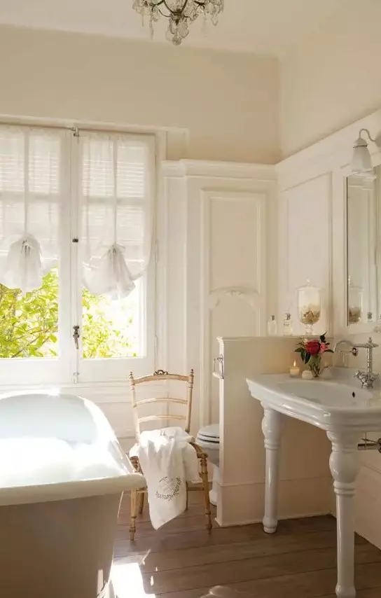a neutral vintage bathroom with a vintage tub, a half wall that separates the toilet zone from the rest of the space, vintage curtains and furniture