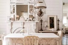 a neutral vintage dining room with white furniture, a vintage lamp, a large mirror and a faux fireplace and a lace tablecloth