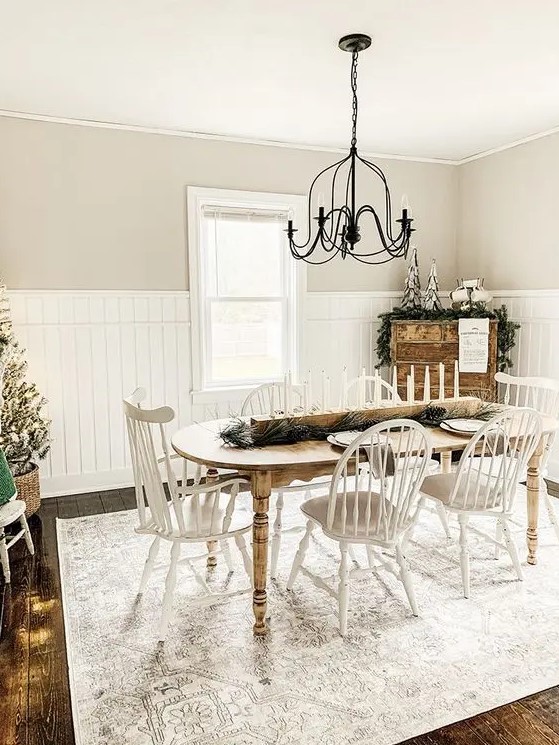 a neutral vintage farmhouse dining room with a curved table, white chairs, a metal chandelier and a wooden dresser