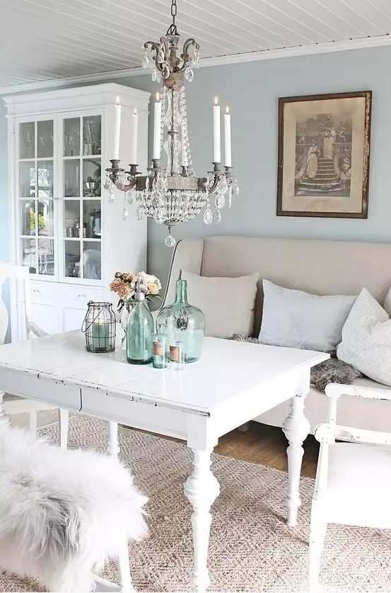 a pastel vintage dining room with blue walls, white shabby chic furniture,a crystal chandelier, blue bottles and jars