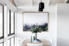 a pretty Scandinavian dining space with a stained table, white chairs, a chic print, black pendant lamps and pastel vases