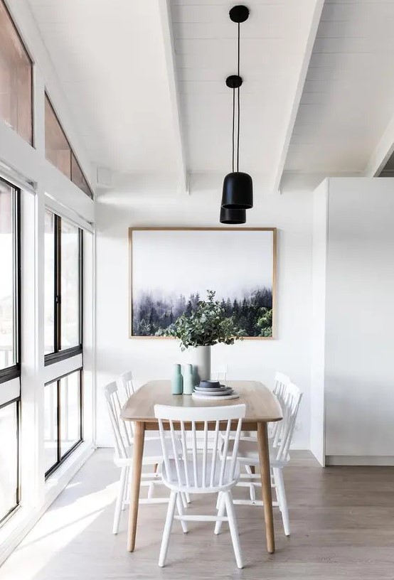 a pretty Scandinavian dining space with a stained table, white chairs, a chic print, black pendant lamps and pastel vases