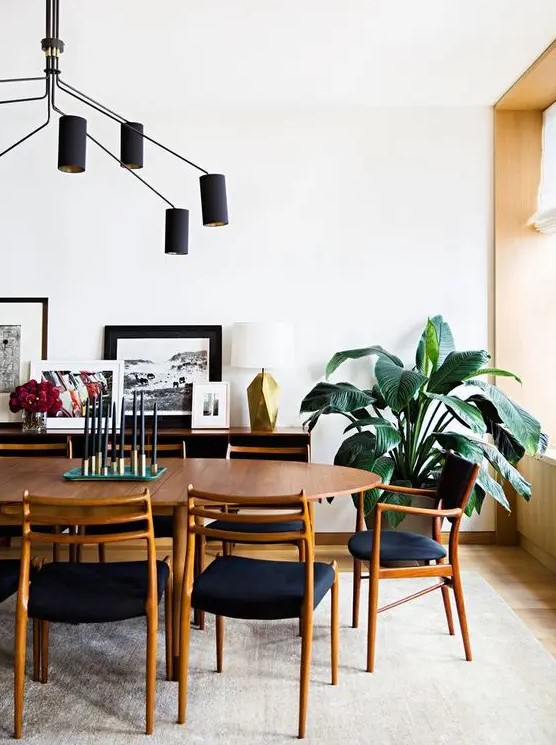 a pretty mid century modern dining room with a stained dining table, navy chairs, a sideboard with a gallery wall and a black chandelier
