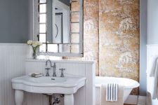 a quirky bathroom with an upholstered accent wall, a vintage tub, a half wall that separates the space and a mirror hanging