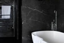 a refined bathroom with black marble walls, a wooden slab floor, a pretty tub and neutral fixtures