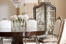 a refined glam dining room in neutral shades, with tan walls, a large floor mirror, a round dark stained table and vintage chairs plus a statement chandelier