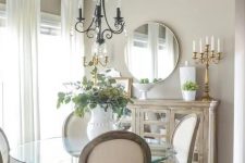 a refined greige dining nook with a reclaimed credenza, a glass round table, white chairs, a vintage chandelier and a chic candelabra
