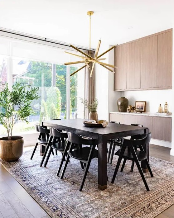 a refined mid century modern dining room with a stained storage unit, a dark stained table and black chairs, a printed rug and a gold chandelier