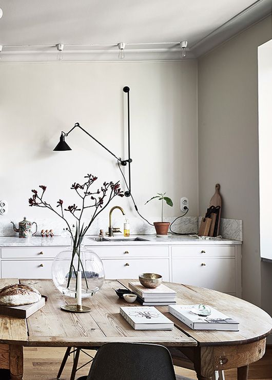 a relaxed Nordic dining space with a wooden table and some chairs, branches in a vase and books is a lovely spot