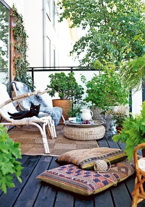 a relaxed boho terrace with rattan furniture, a wicker ottoman, boho pillows, potted greenery and blooms