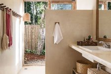 a relaxed indoor-outdoor bathroom with a shower space that is separates with a half wall from the rest of the space