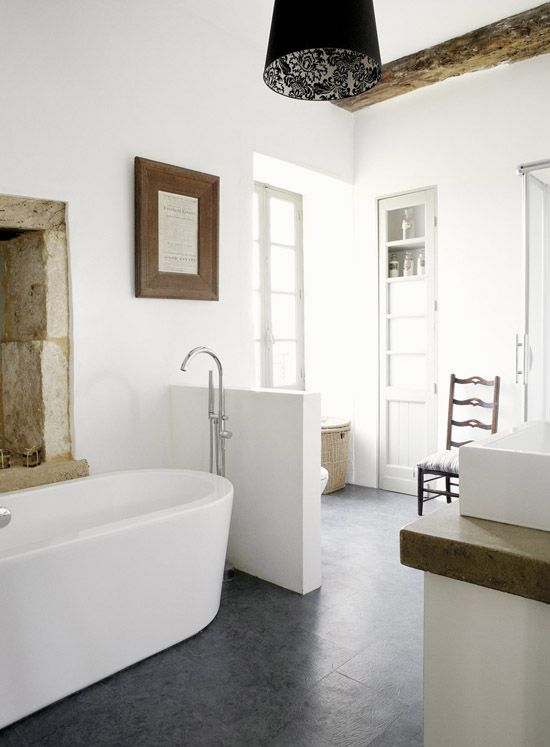 a relaxed neutral bathroom with a wooden beam, an oval tub, a half wall that separates the toilet from the rest of the space