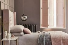 a relaxing and soothing bedroom with taupe walls, a pink upholstered bed with pastel bedding, a pendant lamp and blush solid shutters that match the color of the bed