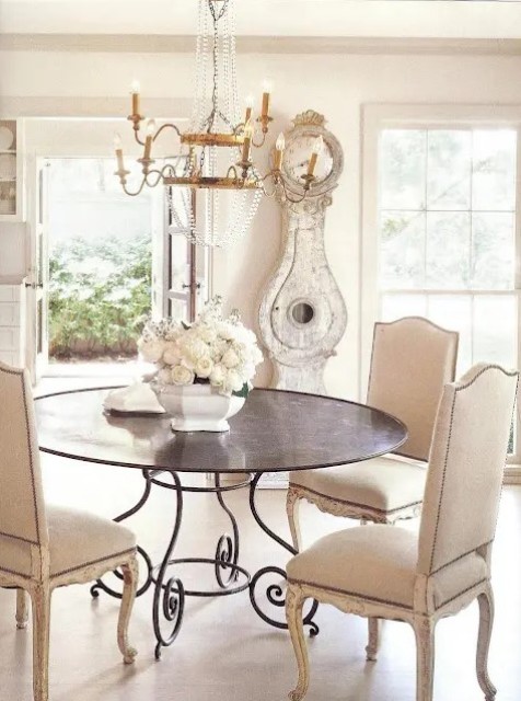 a shabby chic neutral dining room with a metal table, vintage upholstered chairs, a refined crystal chandelier and a whitewashed shabby chic clock