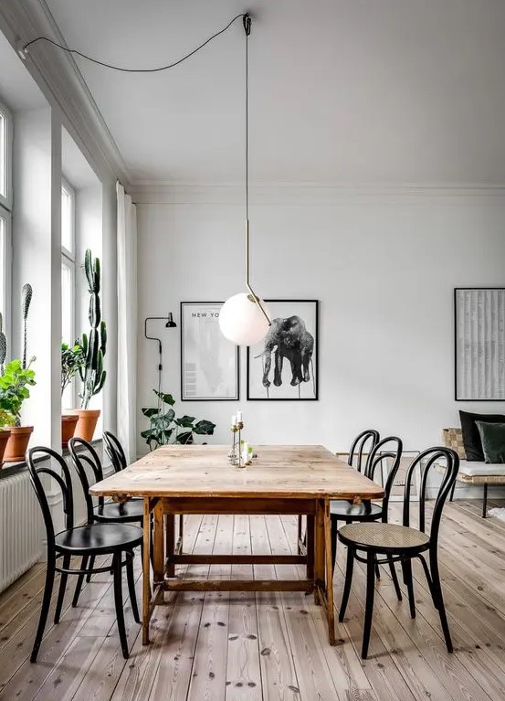 a simple and serene dining space with a stained wooden table, matching chairs, potted plants and a statement pendant lamp