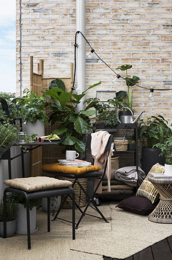 a smal boho terrace with metal furniture, a wooden table, potted greenery, lights and a wooden screen