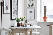 a small Nordic dining area with a folding table, vintage white chairs, a black and white gallery wall and some plants